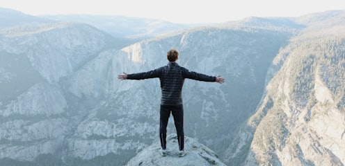 man opening his arms wide open on snow covered cliff with view of mountains during daytime