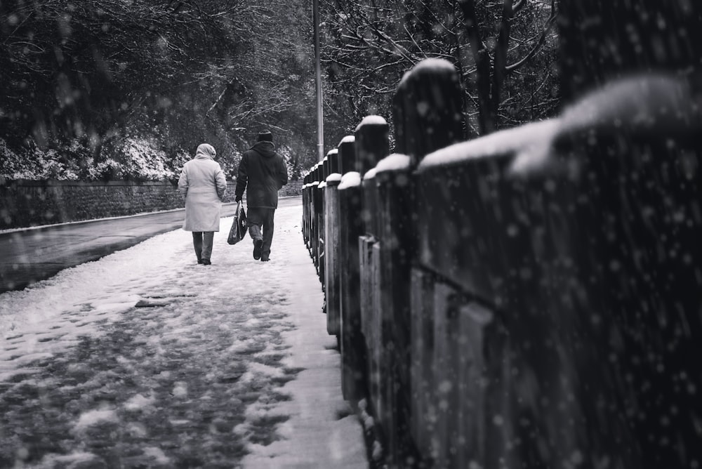 two people walking on sidewalk at the snow