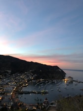 A scenic view of Labuan Bajo harbor at sunset with colorful boats and lush hills.