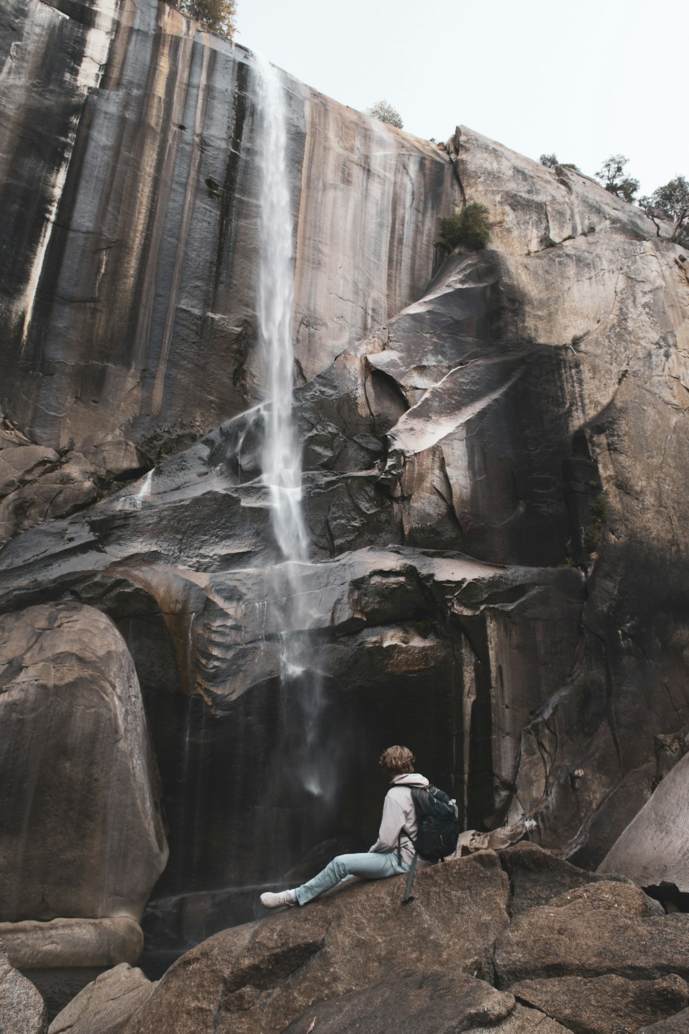 person sitting on rock in front of waterfall