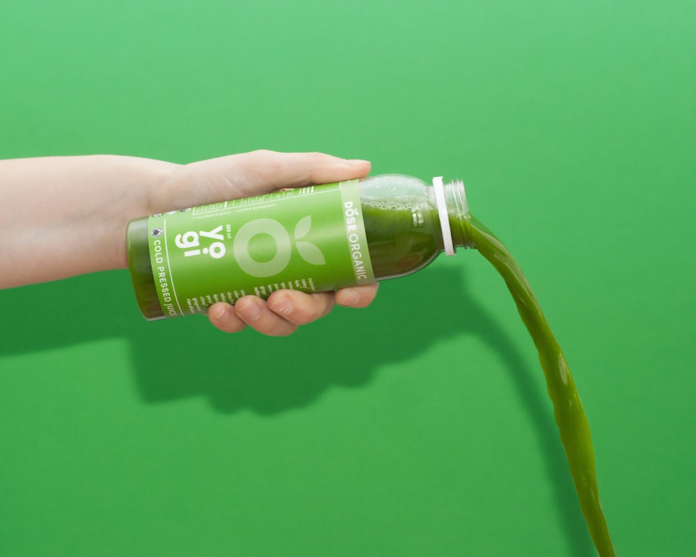 A bottle of green DOSE Juice pours out against a green background
