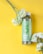 A green bottle labeled 'DOSE ORGANIC' with the word 'cactus' on it is placed on a bright yellow background. Beside the bottle, there are several light green and white flowers, adding a fresh and natural element to the composition.