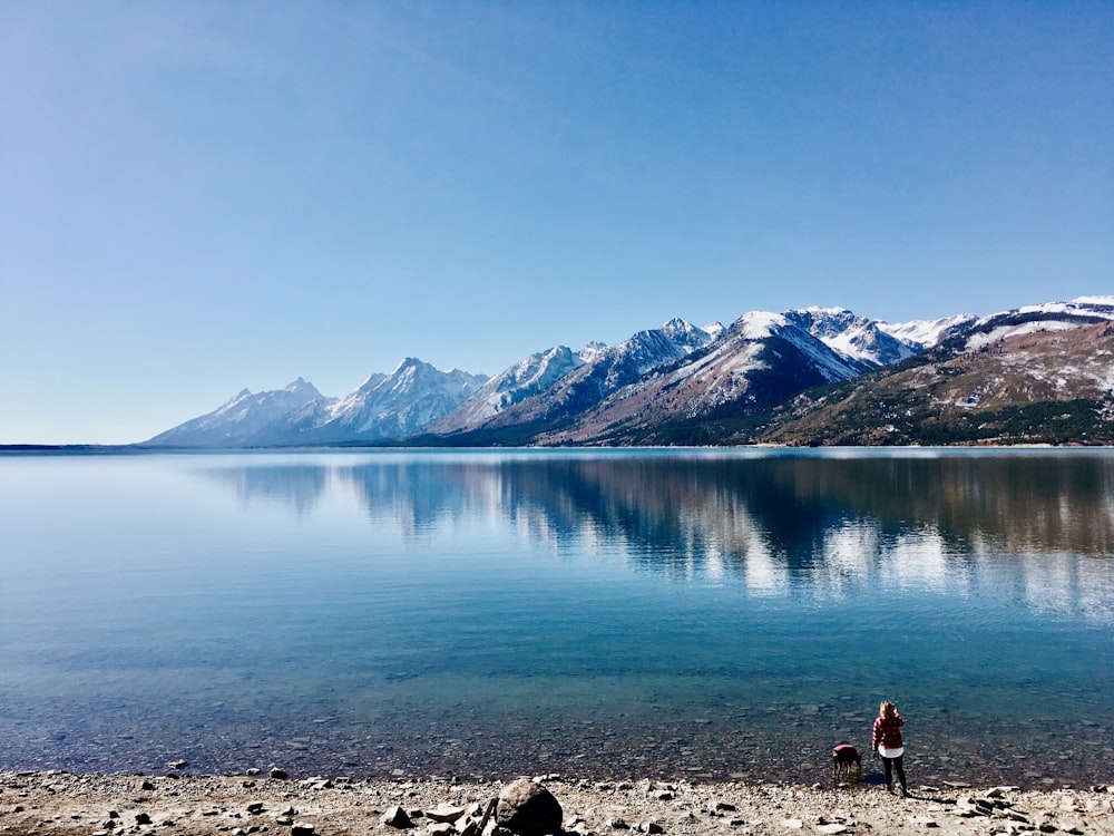 man standing beside body of water with mountain at distance during daytime