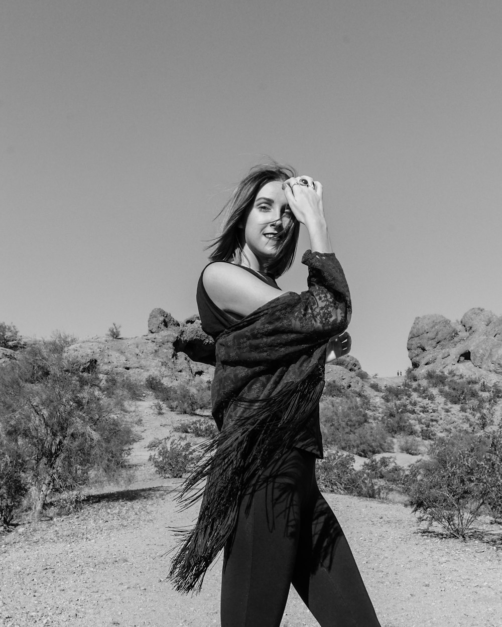 grayscale photo of woman standing near trees and rocks