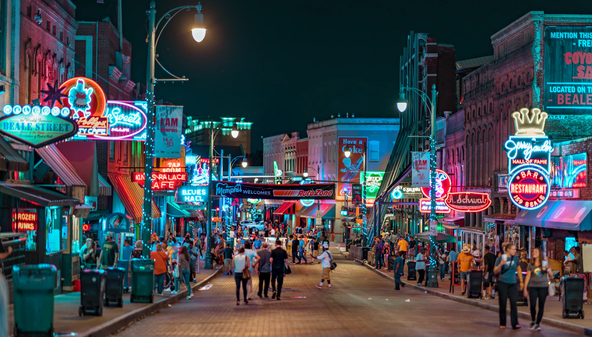 People walking down the middle of a lit street at night, bars glowing on both sides.