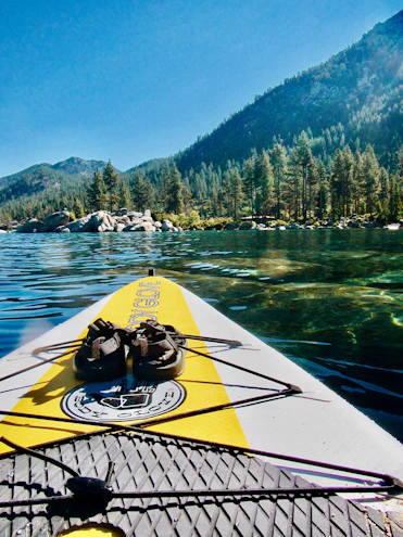 A vibrant inflatable SUP floating on calm lake water with mountains in the background.