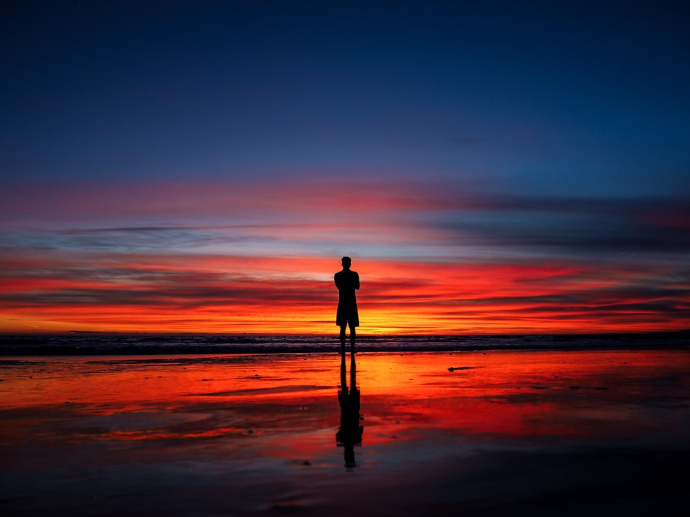 silhouette of man standing on shoreline at night time