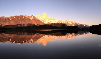 Snow-capped mountains reflecting in a calm alpine lake during golden hour.