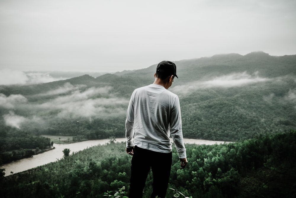 man standing facing forest with river during daytime