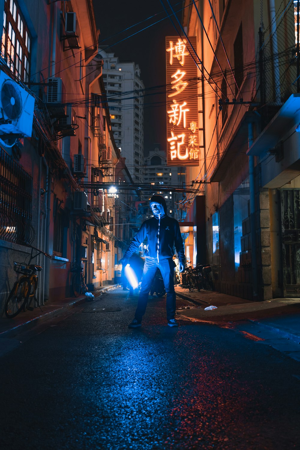 person standing and holding light in between concrete buildings during nighttime