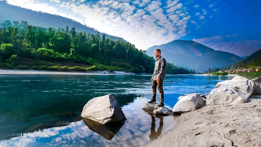 man standing on rocks above body of water overlooking mountains at daytime