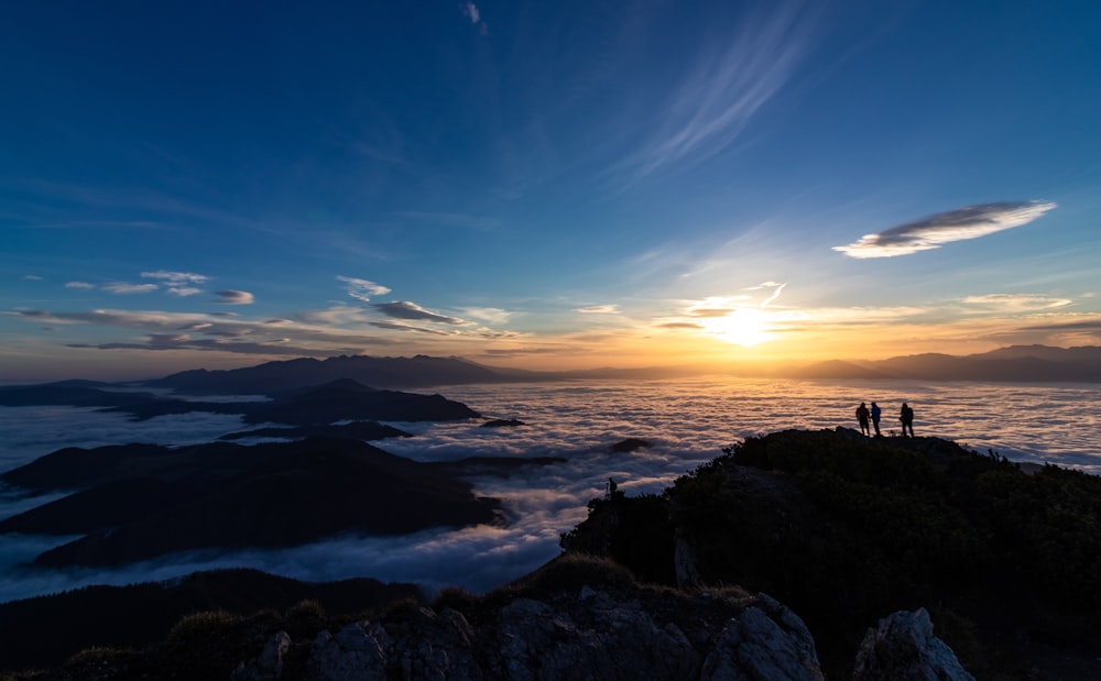 silhouette of three people on sea cliff during golden hour