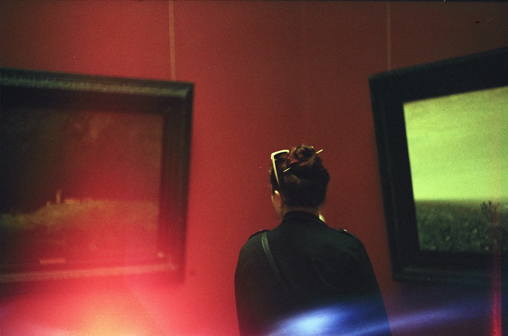 woman standing facing two black wooden framed paintings inside room