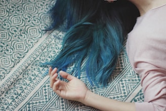 Mulher com cabelo azul caída deitada no tapete branco e verde
