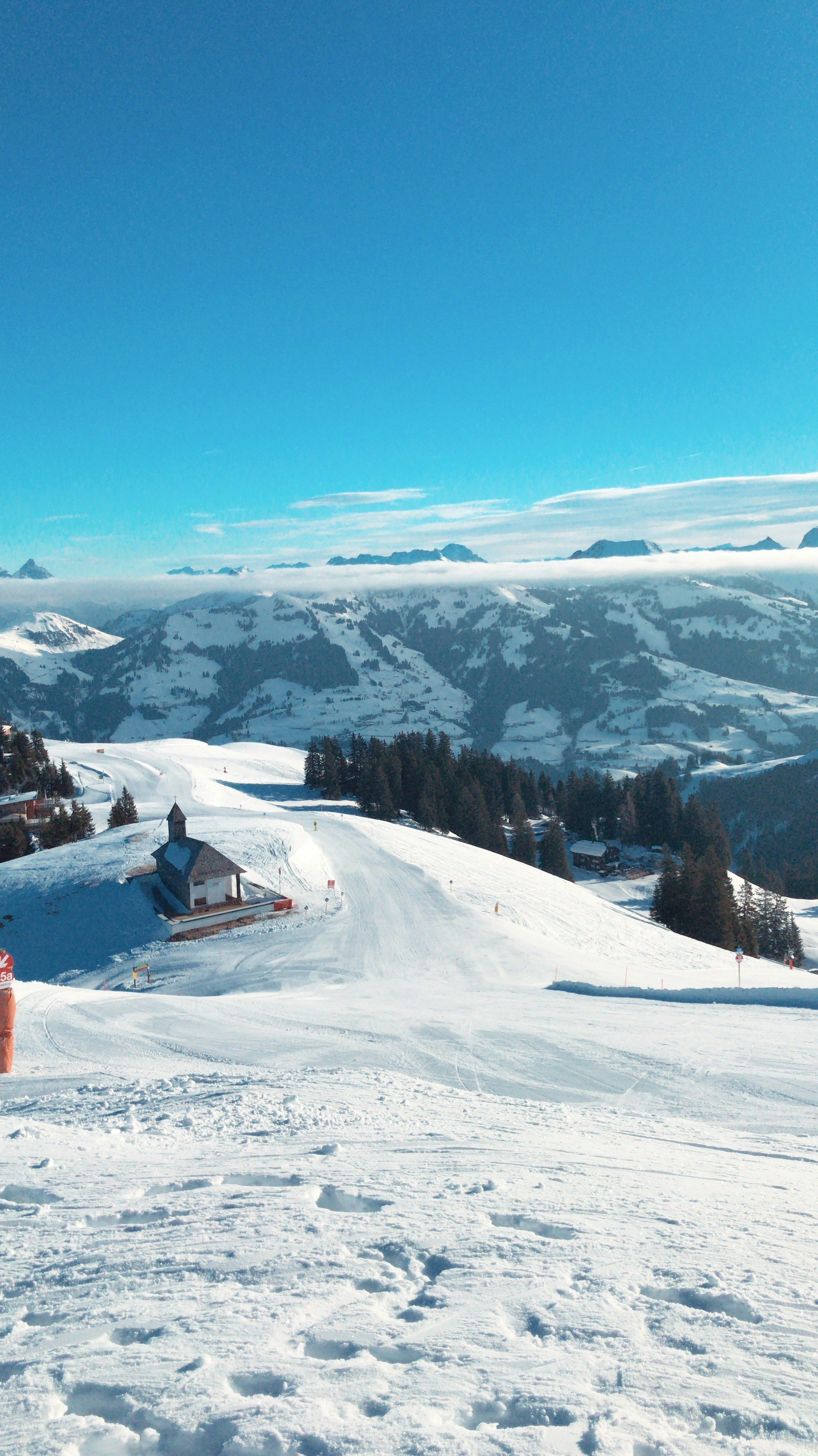 Snow-covered alpine slopes of Kitzbühel with a mountain hut, groomed ski piste, evergreen trees, and