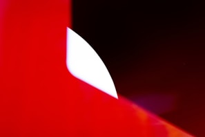 A minimalist composition featuring bold geometric shapes with a strong contrast between bright red and black. A curved white area further adds to the abstract nature of the scene.