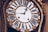 An antique clock with ornate gold detailing and Roman numerals on the clock face. The hands of the clock are elaborately designed, adding to the vintage aesthetic. The clock face has inscriptions in a cursive font.