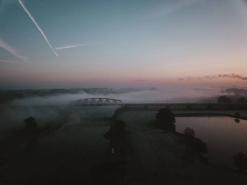 Serene landscape at sunrise with a foggy bridge spanning across a river in mist