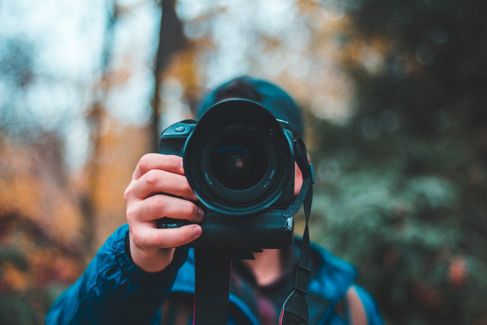 selective focus photography of man holding black DSLR camera