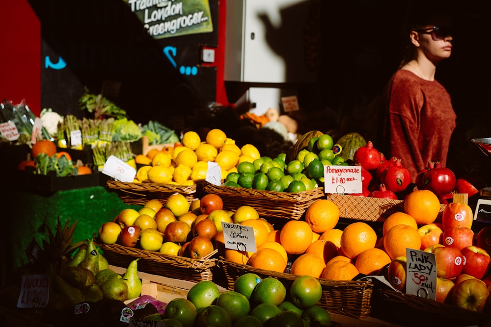 assorted fruits on fruitstand beside woman in brown top