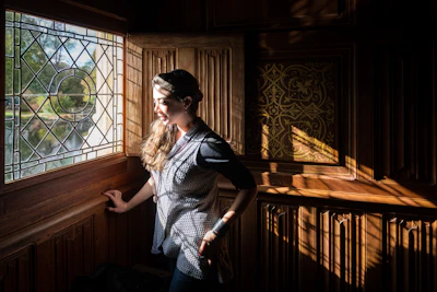 A woman standing by a window, natural light casting gentle shadows on her skin.