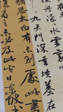 Elegant calligraphy is displayed on textured paper with vertical and diagonal orientations. The script appears in bold black ink against creamy beige and muted gold backgrounds, creating a contrast that highlights the artistry and fluidity of the characters.