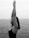 A woman is practicing yoga by the sea, standing with arms raised and eyes closed, conveying a sense of calmness and introspection.
