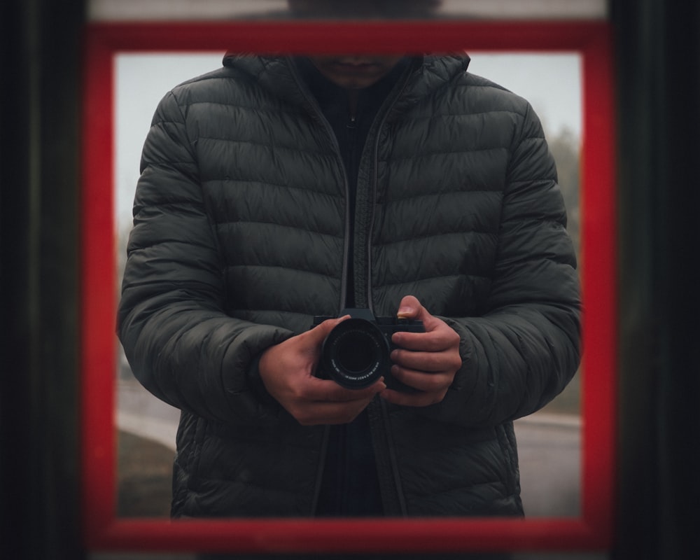 man wearing black bubble jacket holding DSLR camera