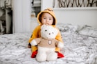 toddler sitting on bed beside white bear plush toy