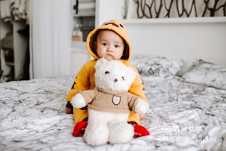 toddler sitting on bed beside white bear plush toy