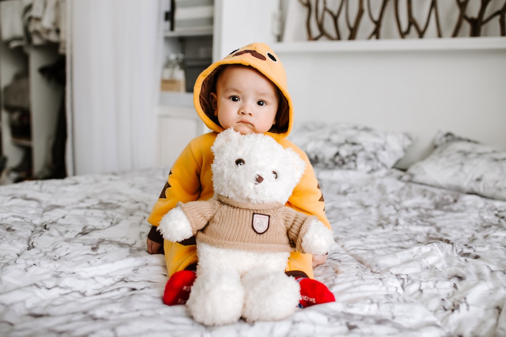 toddler sitting on bed beside white bear plush toy