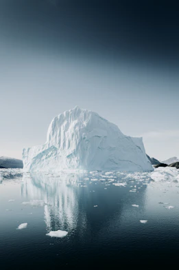 A large white iceberg reflected in the calm dark water of the Arctic