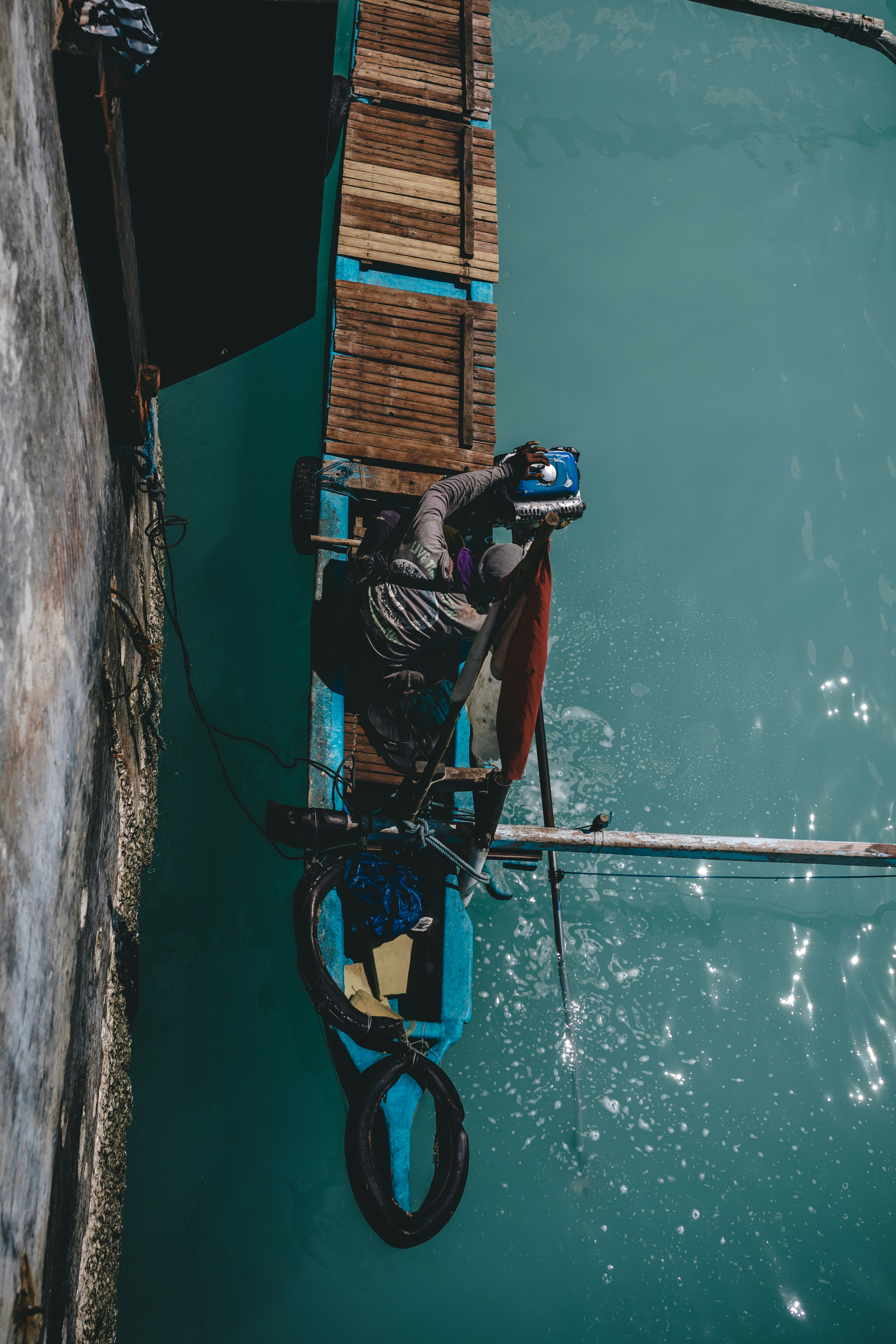 Un homme répare un moteur hors-bord sur un bateau en bois.
