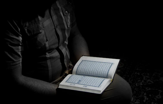 A person holding an illuminated Bible with soft light emanating in a dark room.