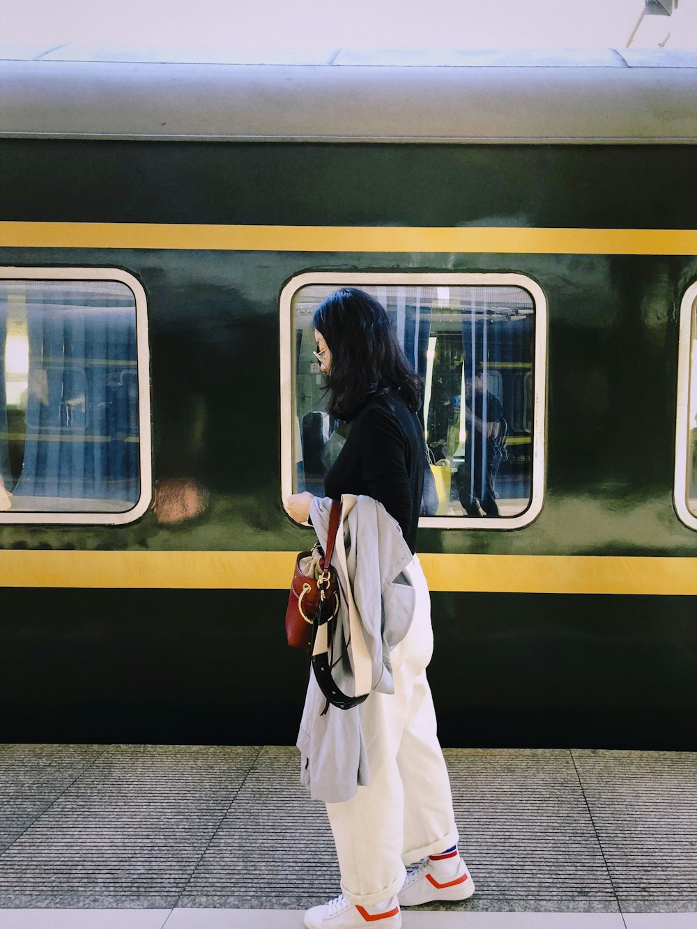 woman standing holding red bag near train