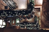 A detailed view of a decorated interior with garlands of green foliage and small white lights draped over the banisters. Marble and intricate woodwork add to the elegant architectural setting. The warm ambient lighting creates a festive and inviting atmosphere.