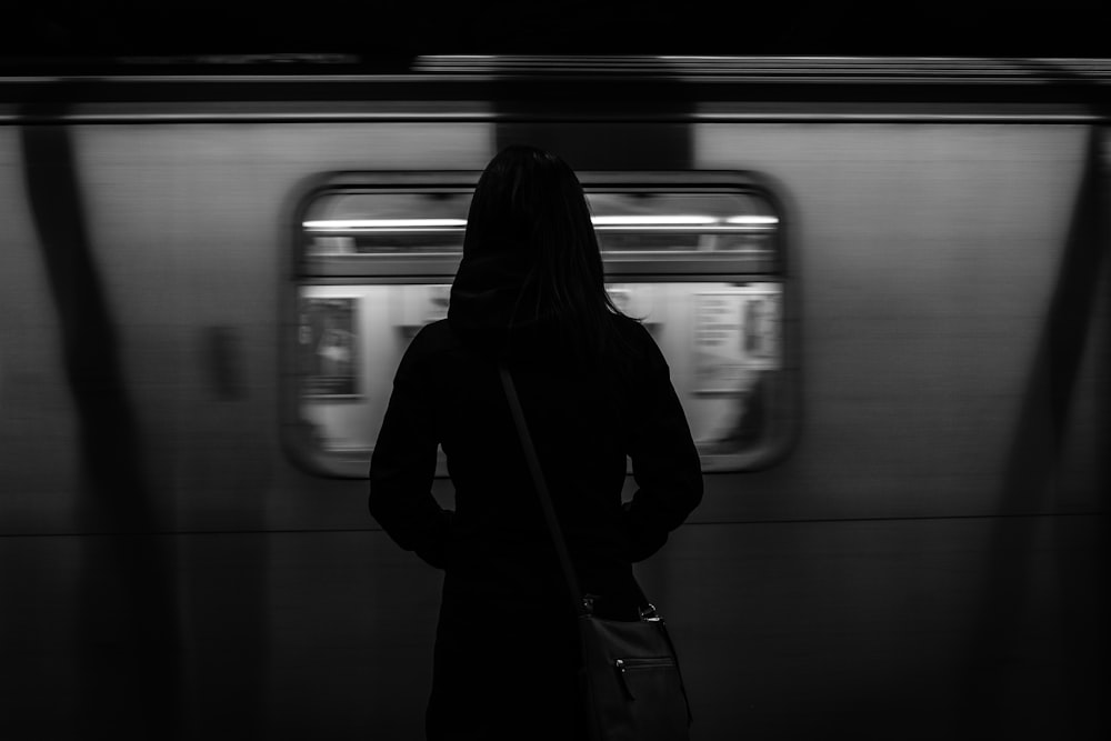 grayscale photography of woman standing near running train