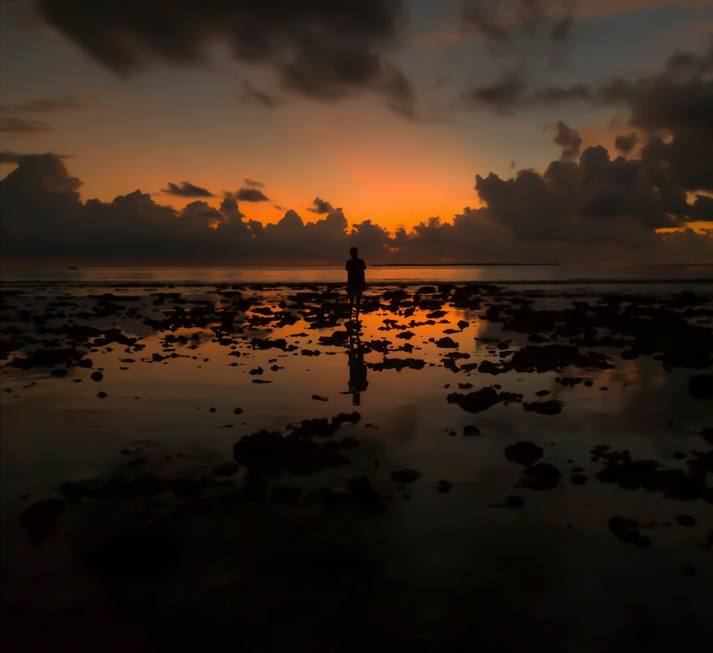 silhouette of person standing on rocks on sea