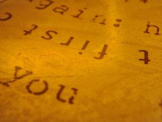 An abstract close-up of text on a paper with a warm, golden hue. The text appears reversed and slightly blurred, creating an artistic and mysterious effect.
