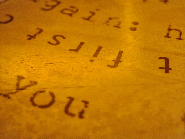 An abstract close-up of text on a paper with a warm, golden hue. The text appears reversed and slightly blurred, creating an artistic and mysterious effect.
