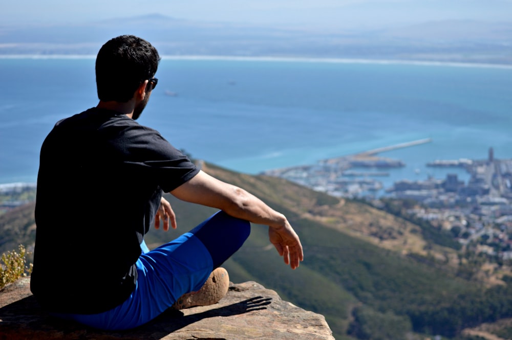 man in black shirt and blue bottom sitting on rock