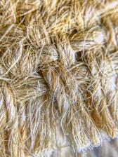 A close-up view of a textured, woven fiber material with tightly interwoven strands. The fibers appear soft yet robust, with a natural, earthy hue.