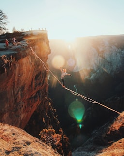 man walking on string hanging from rock mountains