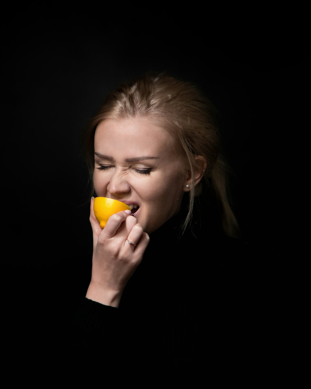 woman in black long-sleeved top eating lemon