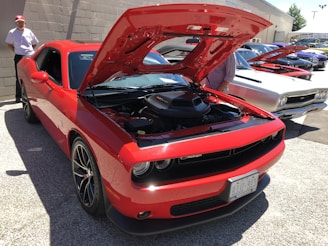 A vibrant red, white, and blue classic American muscle car displayed at an outdoor car show under a bright sunny sky.