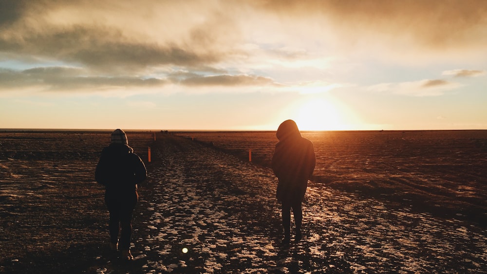 two person standing on brown field during sunset