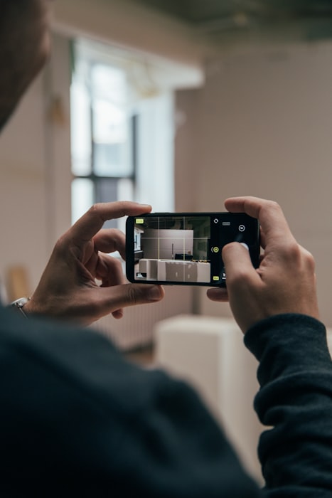 A person holds a smartphone while filming a product on a table, representing the UGC capture step that feeds Instagram and product-page shoppable video alike.