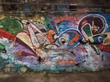 Colorful graffiti covers a textured stone wall, featuring a mix of abstract shapes and vibrant patterns in shades of green, red, blue, and orange. The words 'Istanbul' and 'KUNSTSTOFF' are visible among the designs.