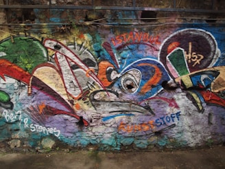 Colorful graffiti covers a textured stone wall, featuring a mix of abstract shapes and vibrant patterns in shades of green, red, blue, and orange. The words 'Istanbul' and 'KUNSTSTOFF' are visible among the designs.