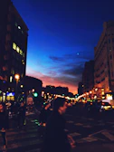 A bustling city street at dusk with glowing lights and people walking.
